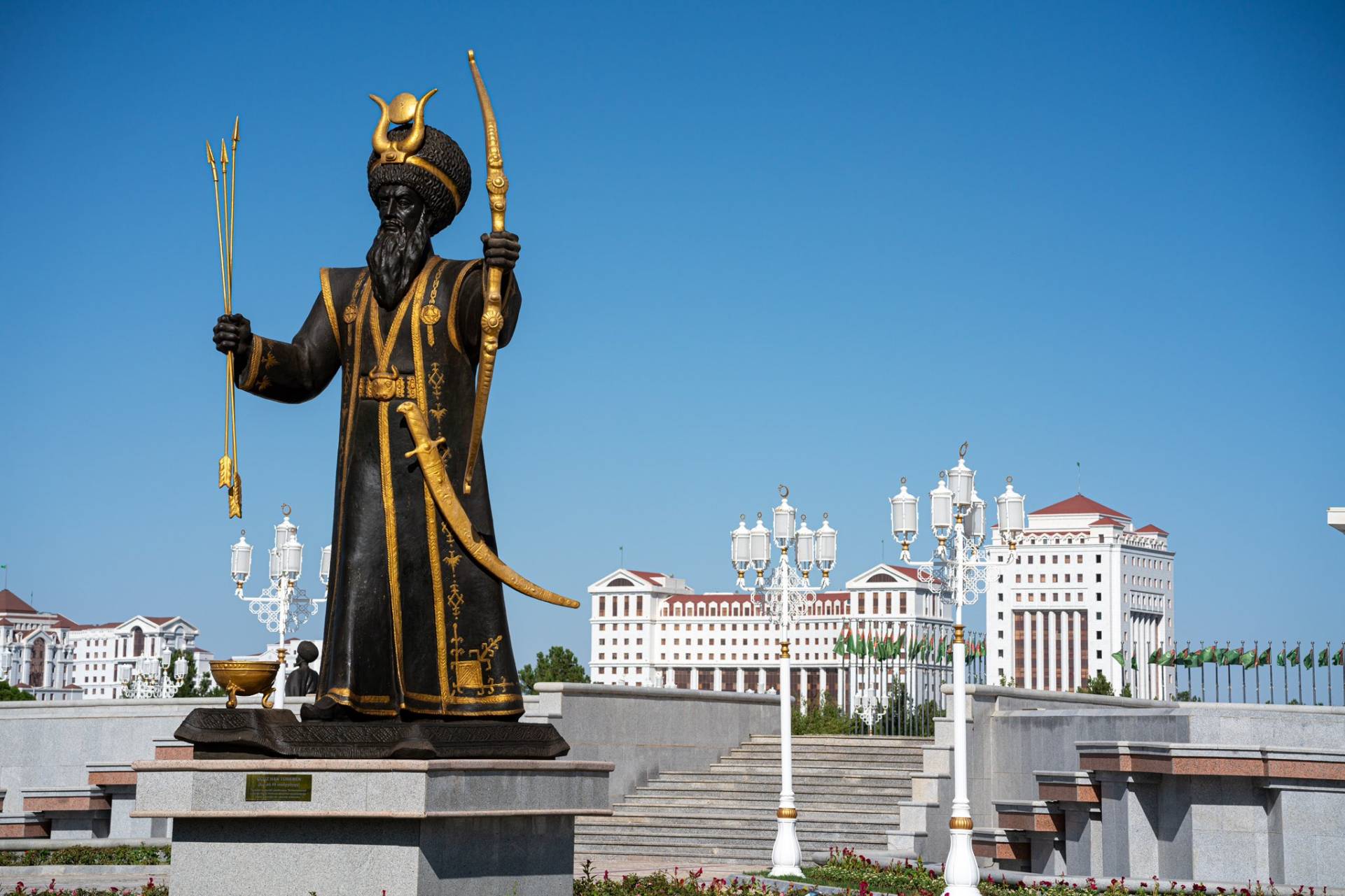 2 Day Turkmenistan Tour from Bukhara: Merv & Ashgabat Statue of a warrior with bow and arrows in Ashgabat, Turkmenistan, with white marble buildings in the background.