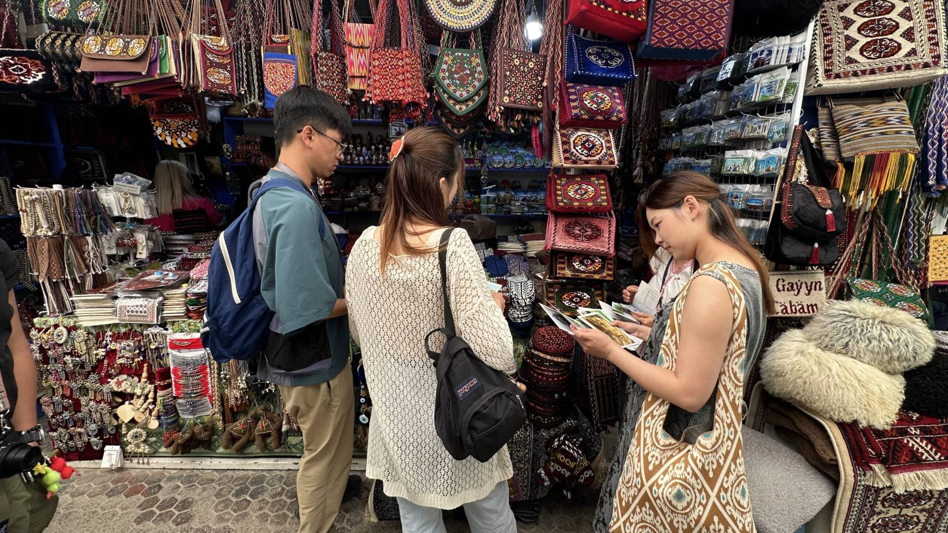 4 Day Turkmenistan Tour: Farab to Shavat via Merv, Ashgabat & Darvaza Japanese tourists shopping for traditional Turkmen souvenirs, carpet bags and handicrafts at the Russian Bazaar in Ashgabat