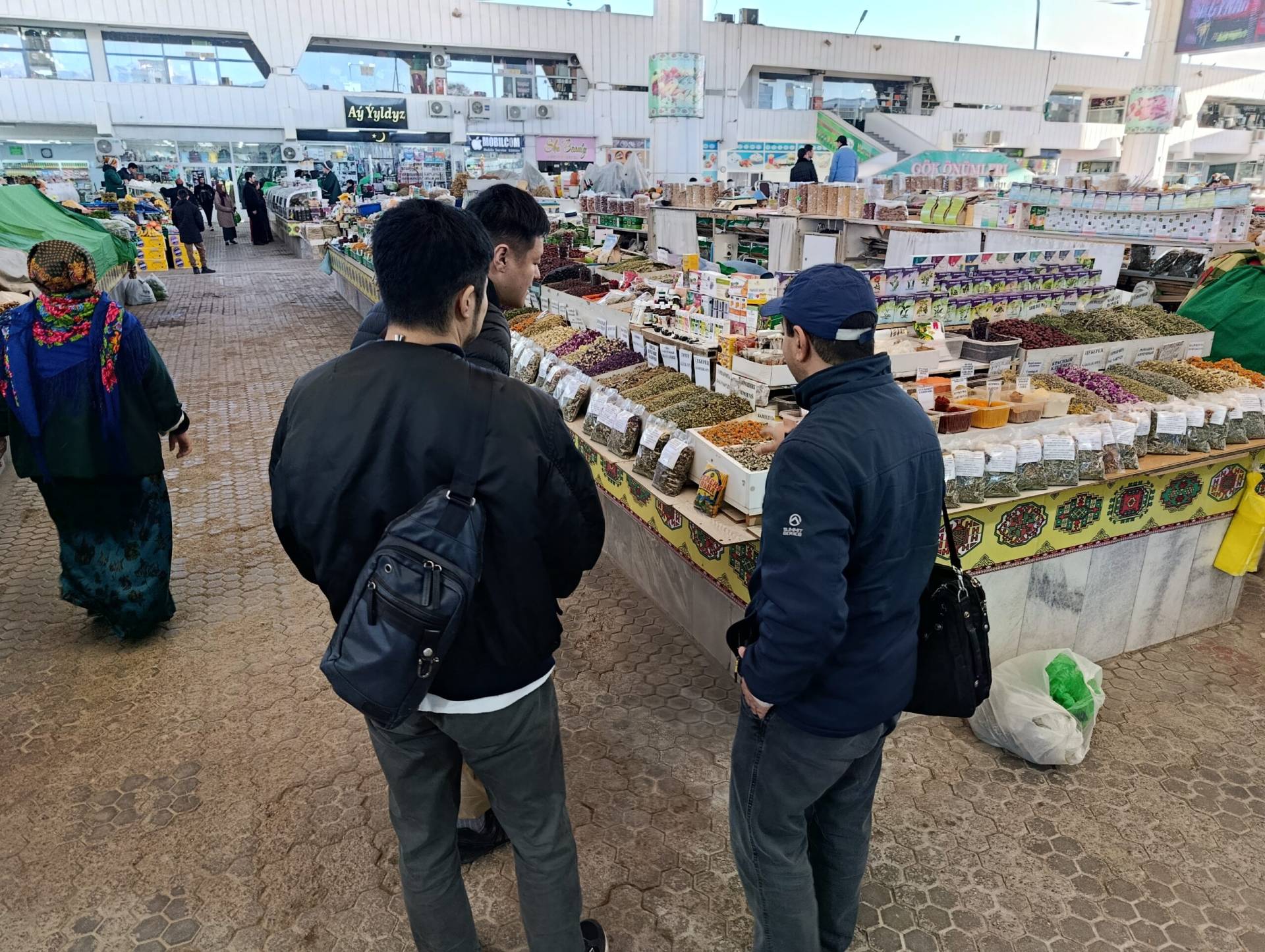 1 Day Turkmenistan Tour from Khiva: Dashoguz & Kunya-Urgench Japanese tourists and their guide exploring traditional herbs and spices at the Russian Bazaar in Ashgabat
