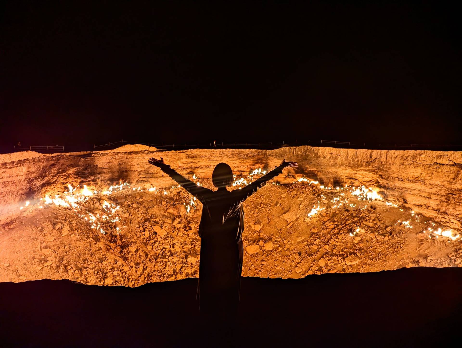 3 Day Turkmenistan Tour from Ashgabat: Darvaza & Night Train to Bukhara Tourist raising arms in front of the burning Darvaza Gas Crater at night in Turkmenistan