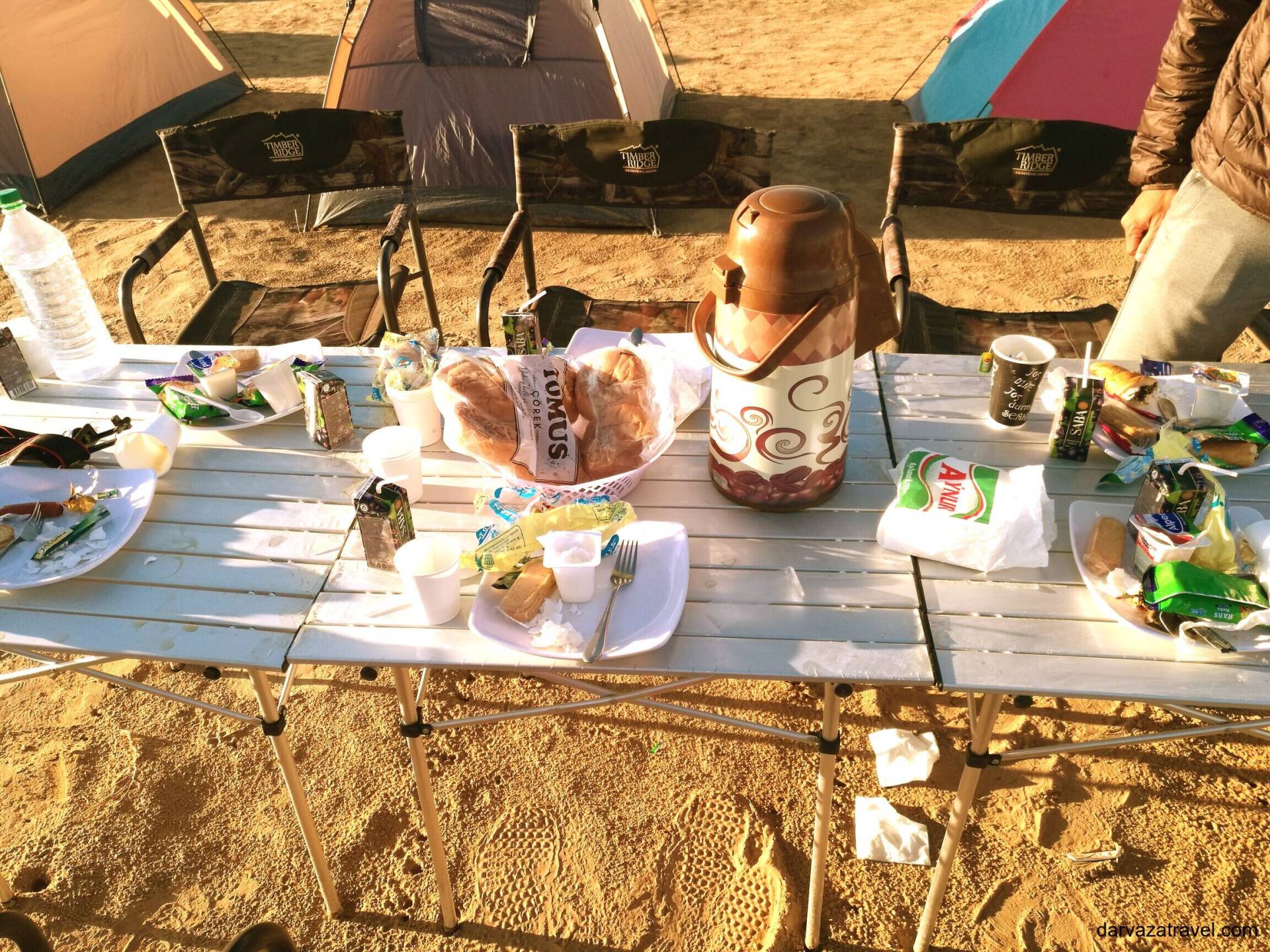 Darvaza Yurt Camp Desert breakfast table with bread, snacks, tea thermos, and disposable plates at Darvaza Yurt Camp