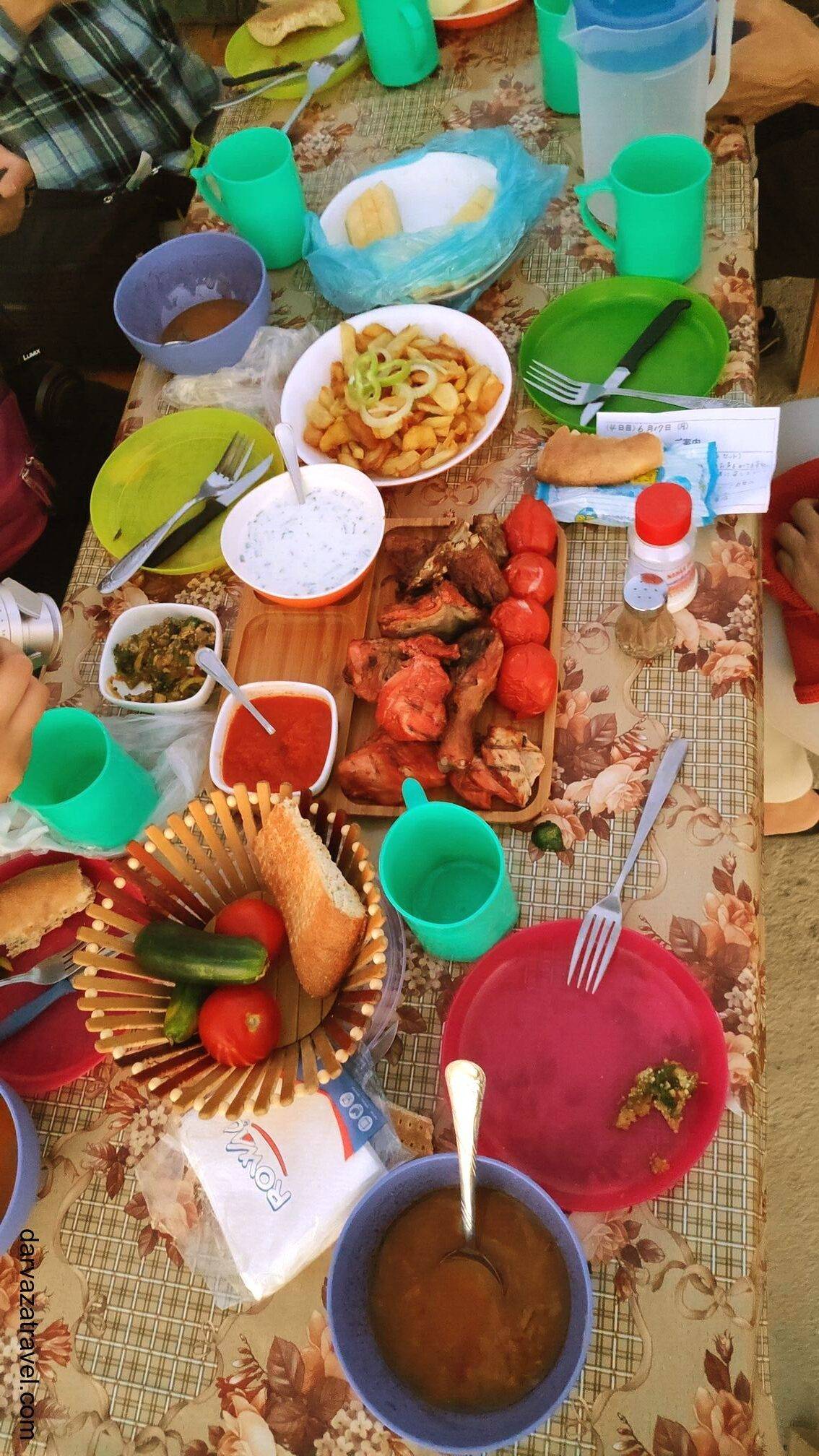 Darvaza Yurt Camp Dinner table with kebabs, bread, tomatoes, cucumbers, and plastic utensils at Darvaza Yurt Camp