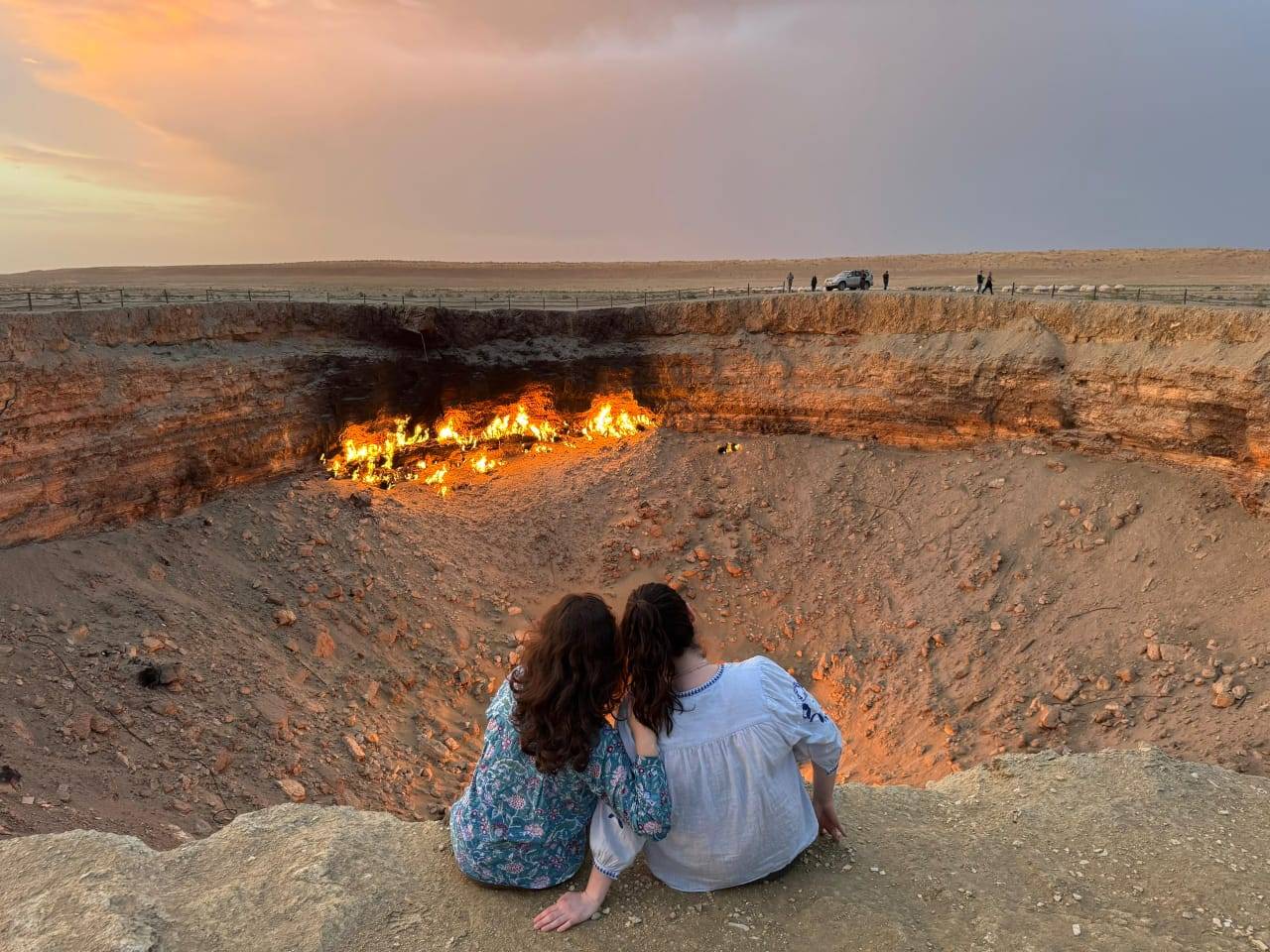 4 Day Turkmenistan Tour: Farab to Shavat via Merv, Ashgabat & Darvaza Two travelers sitting beside the burning Darvaza Gas Crater at sunset in Turkmenistan
