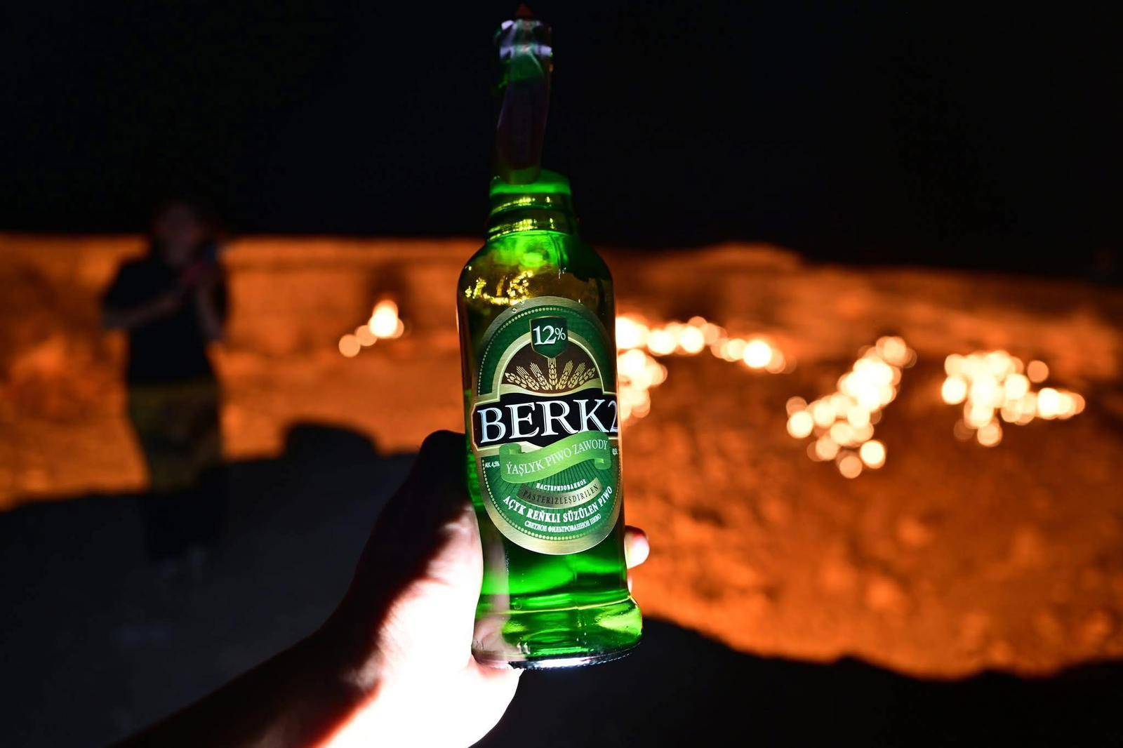 2 Day Turkmenistan Tour from Khiva to Darvaza Gas Crater Turkmen beer bottle held in front of the burning Darvaza Gas Crater in Turkmenistan at night