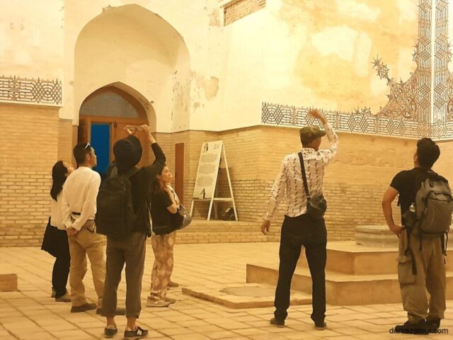 Travelers photographing and admiring traditional Turkmen architecture with decorated walls and arched doorway during guided tour in Turkmenistan