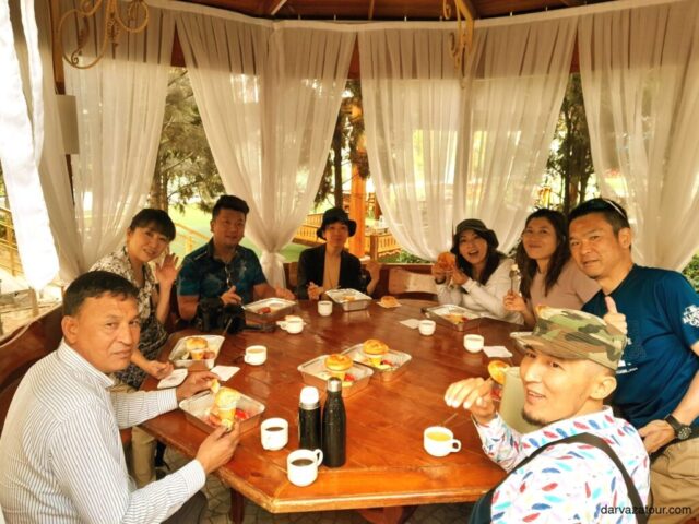 Delicious Turkmenistan breakfast with fresh yogurt and sausage eggs served at luxury hotel in Turkmenistan. Tourists enjoying authentic Central Asian cuisine in beautiful garden pavilion with white curtains. Darvaza tour group travel experience.