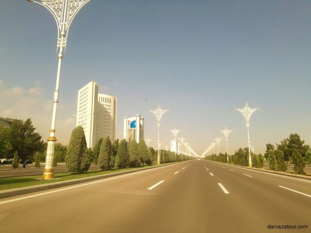 Modern boulevard in Ashgabat, Turkmenistan, featuring white marble buildings, decorative street lamps, and manicured greenery characteristic of the capital city known as the White Marble City