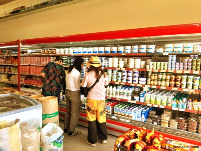 Tourists browsing dairy section at Turkmenistan local market purchasing yogurt and Ayran drinks for road journey