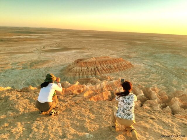 Visitors photographing the colorful rock formations of Yangikala Canyon during golden hour in Turkmenistan's natural landscape