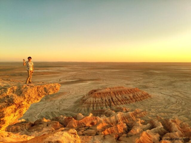 Tourist enjoying panoramic view of colorful rock formations at Yangikala Canyon in Turkmenistan during golden hour