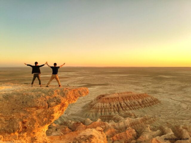 Travelers enjoying sunset view at Yangikala Canyon in Turkmenistan, colorful rock formations, dramatic desert landscape, Turkmen natural landmark