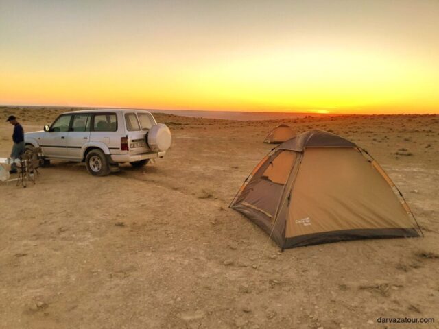 Tourist camping with tent and vehicle at Yangikala Canyon during sunset in Turkmenistan, showcasing adventurous accommodations during a 20-day itinerary across the country