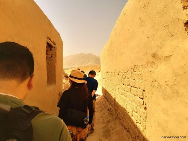 Tourists exploring ancient Nissa ruins in Turkmenistan, walking along narrow passageways between tall clay walls illuminated by warm sunlight