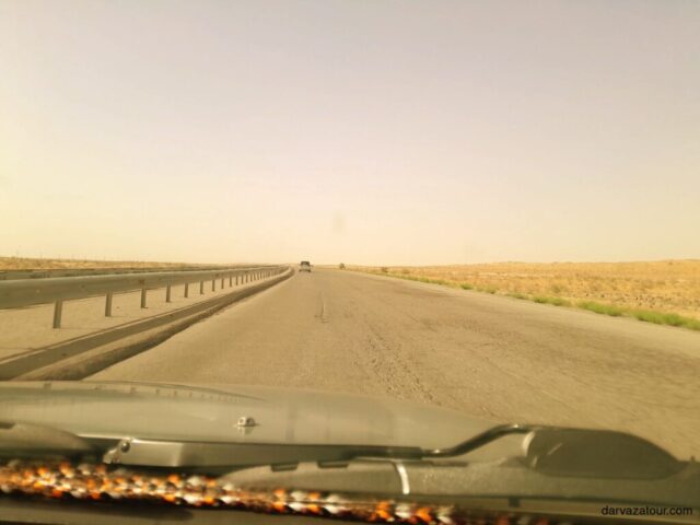 Scenic desert highway in Turkmenistan on the journey to Darvaza Gas Crater, empty road stretching to the horizon with vast barren landscape on both sides, authentic travel experience with Darvaza Tour