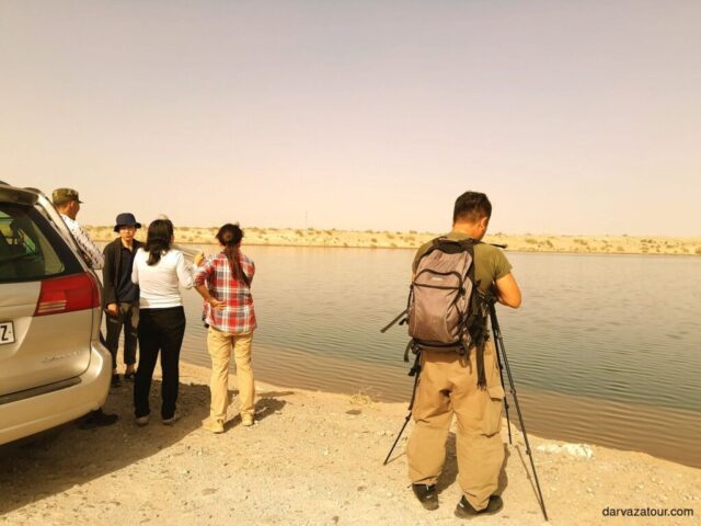 Tourists enjoying the view of a lake in Turkmenistan during their journey with Darvaza Tour. The group is standing on the shore, photographing the picturesque landscape at sunset.