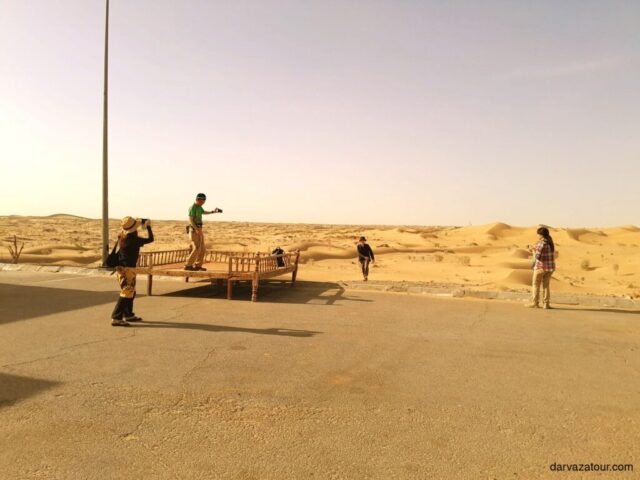 Tourists rest in a desert oasis of Turkmenistan during an excursion to the Darvaza crater. Travelers take photos and enjoy the unique landscape of sand dunes under the soft evening sun.