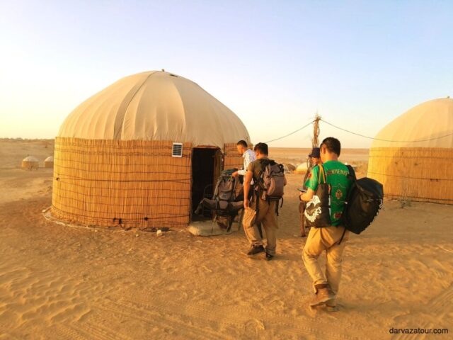 Traditional Turkmen yurts near the Darvaza Gas Crater in the Karakum Desert, tourists with backpacks arriving for overnight stay, ecotourism in Turkmenistan, unique desert living experience near the Gates of Hell