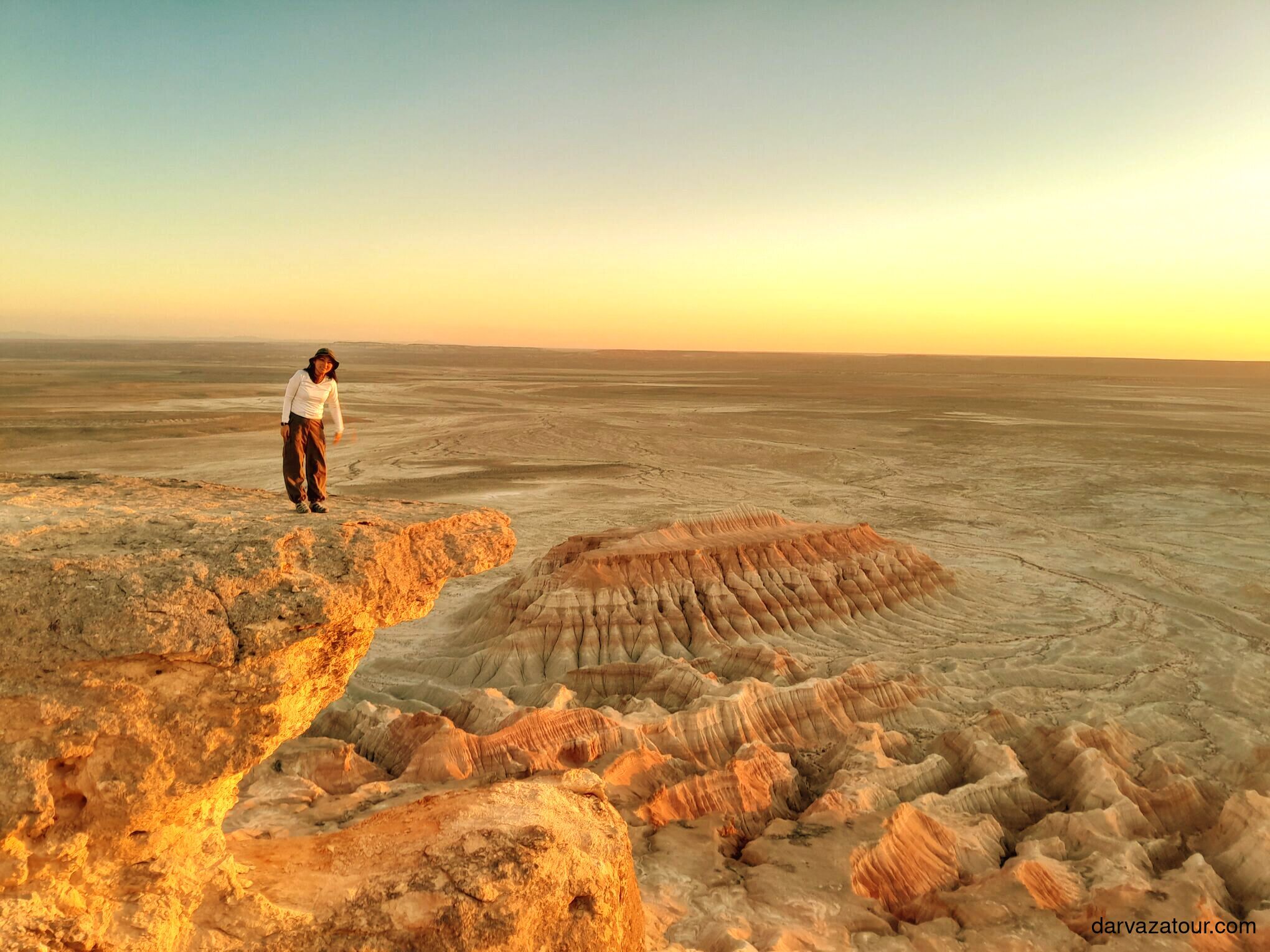 Woman standing near the edge of Yangikala Canyon at sunset, overlooking dramatic rock formations
