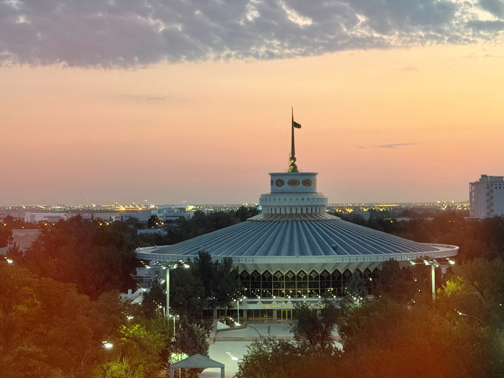 Ashgabat State Circus building illuminated during sunset with the Turkmenistan flag above the circular roof