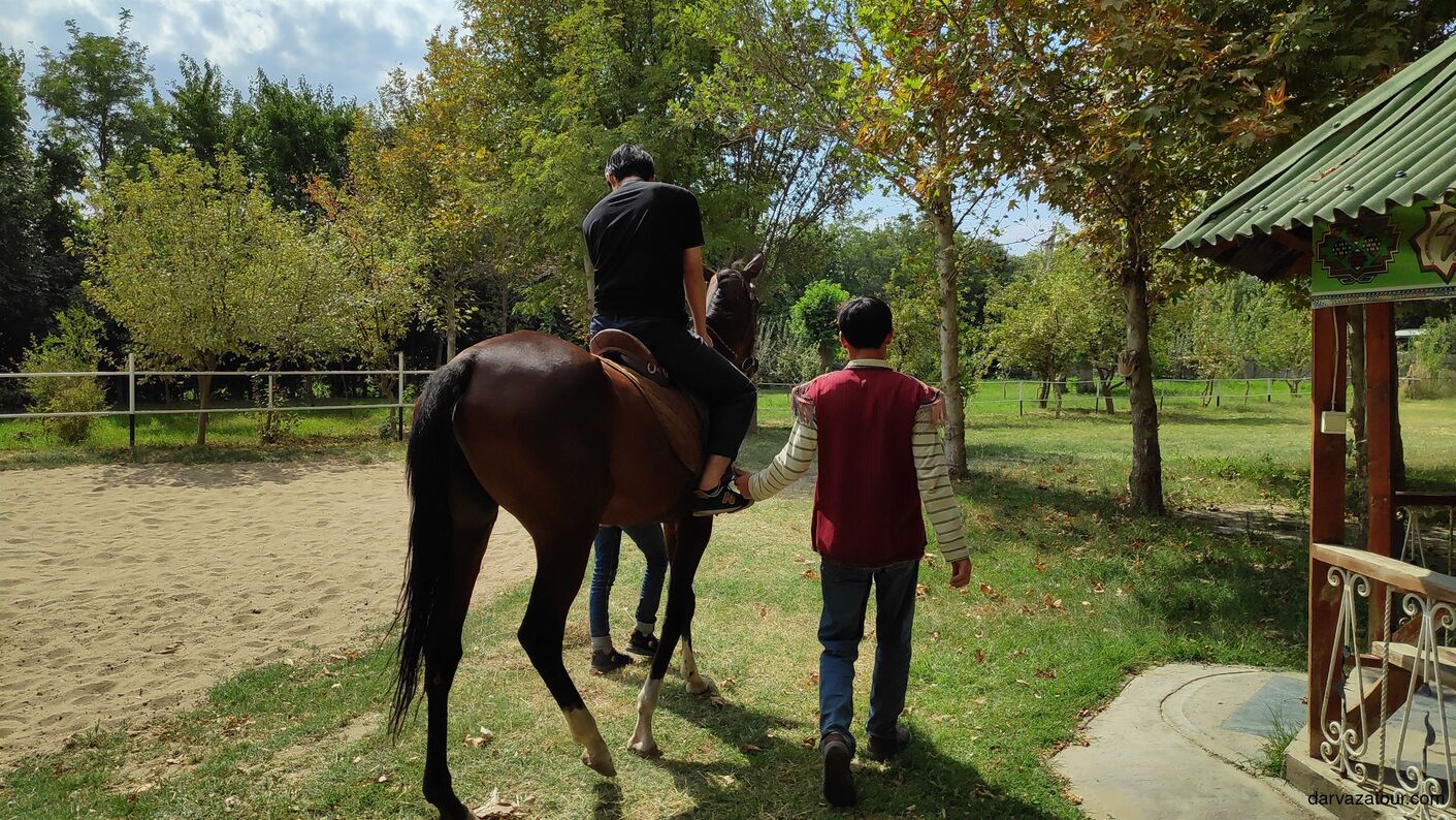 Japanese tourist riding an Akhal-Teke horse at Bede farm in Turkmenistan, guided by local horseman