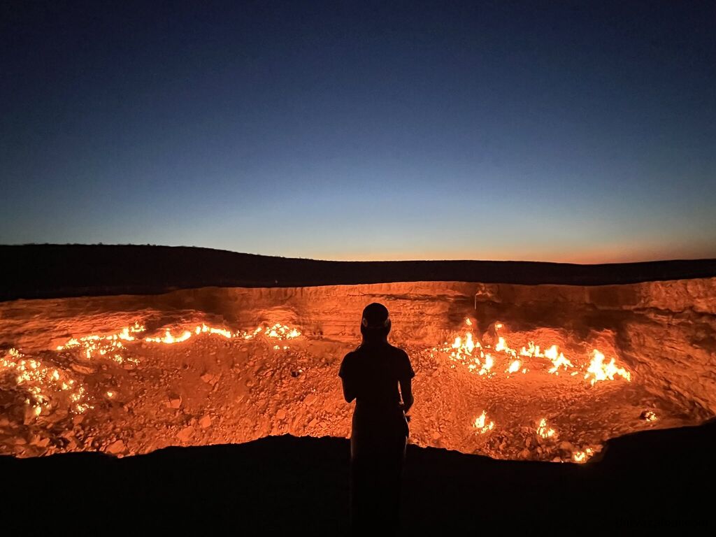 Tourist watching the burning Darvaza Gas Crater at sunset in Turkmenistan