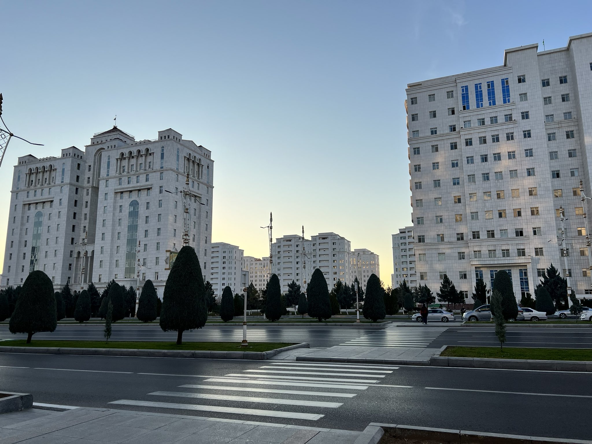 White marble buildings and tree-lined avenue in Ashgabat, Turkmenistan, at sunset.