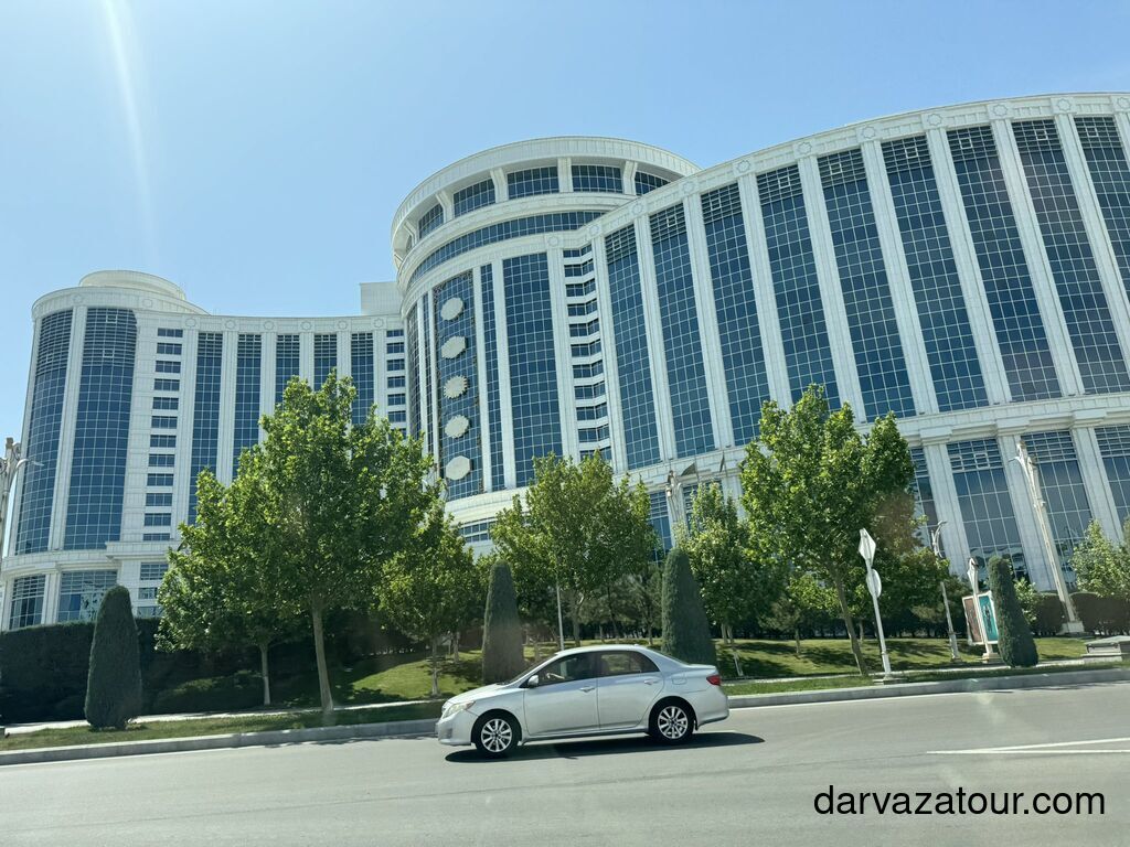 Sport Hotel in Ashgabat, Turkmenistan, a modern four-star building with large glass windows, trees in front, and a white Toyota sedan passing by on the main street.