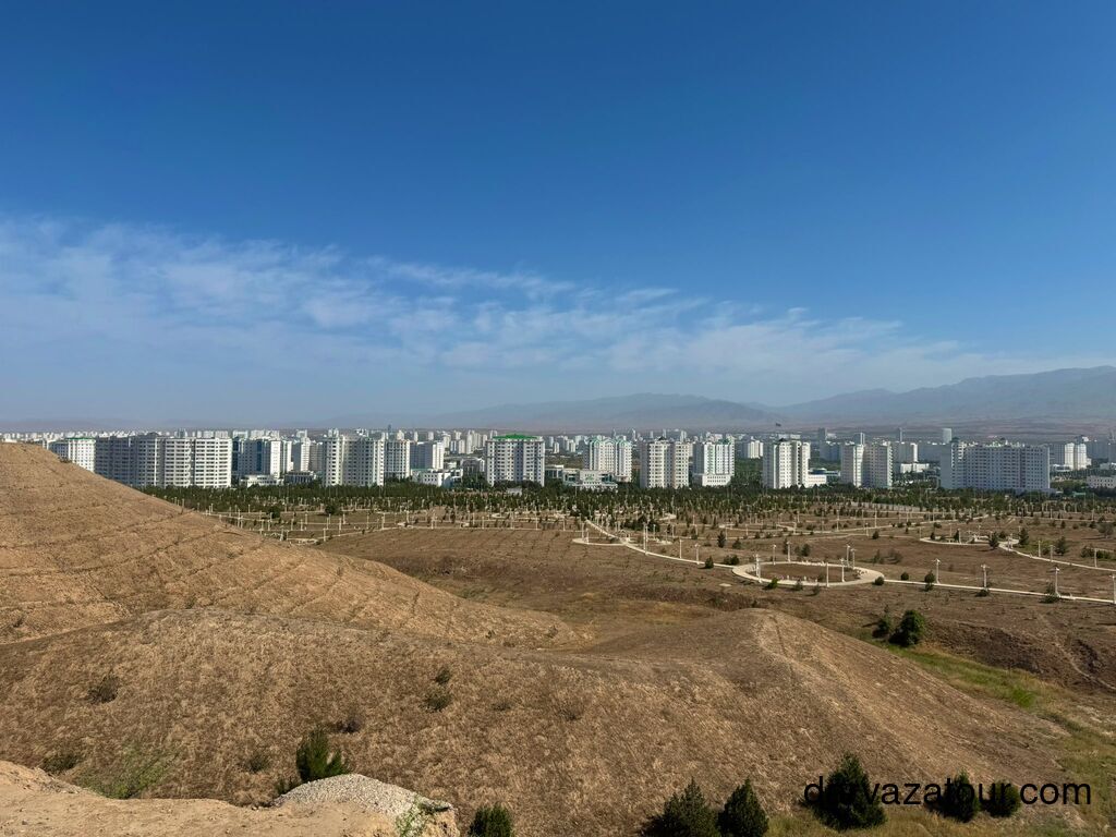 Panoramic view of Ashgabat, Turkmenistan, showing the city’s white marble buildings surrounded by dry hills and green park areas, photographed from an elevated point near a hotel.