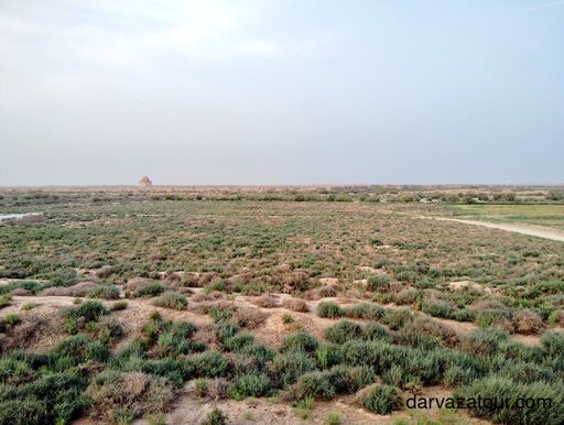 View of Sultan Sanjar Mausoleum from Kyz Kala in ancient Merv, Turkmenistan – wide desert landscape with green vegetation under soft evening sky