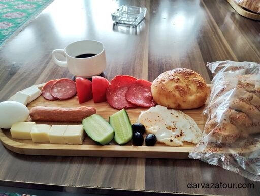 Traditional hotel breakfast in Ashgabat by Darvaza Tour – eggs, cheese, sausage, bread, olives, vegetables, and coffee