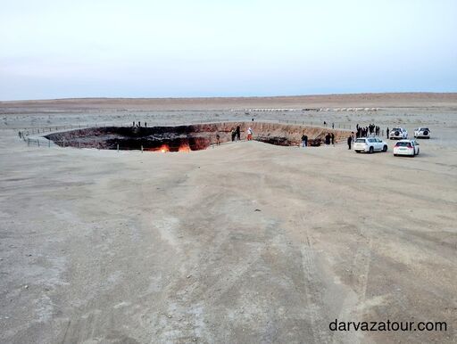 Morning view of the Darvaza Gas Crater in Turkmenistan desert with tourists and 4x4 cars around the burning crater