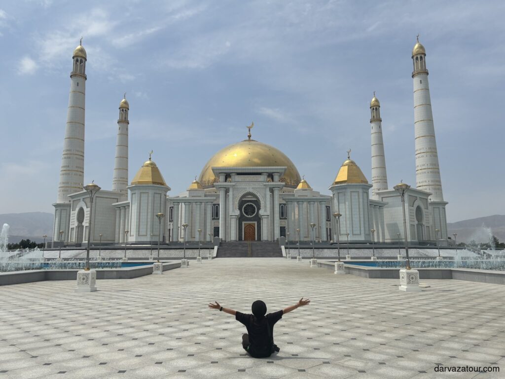 Tourist sitting in front of Gypjak Mosque (Turkmenbashi Ruhy Mosque) with golden domes in Ashgabat, Turkmenistan