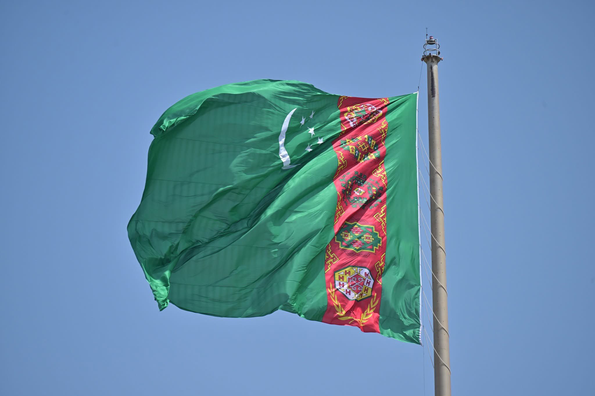 Turkmenistan national flag waving on a tall flagpole against blue sky