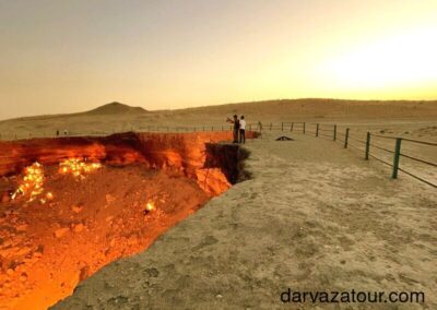 Scenic view of the Darvaza Gas Crater at sunset with desert landscape and a person observing, Turkmenistan