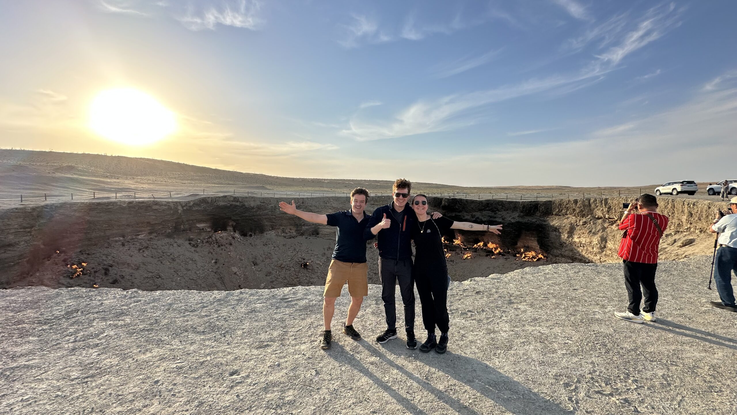 Three travelers from Syria posing beside the Darvaza Gas Crater in the morning during their Turkmenistan tour