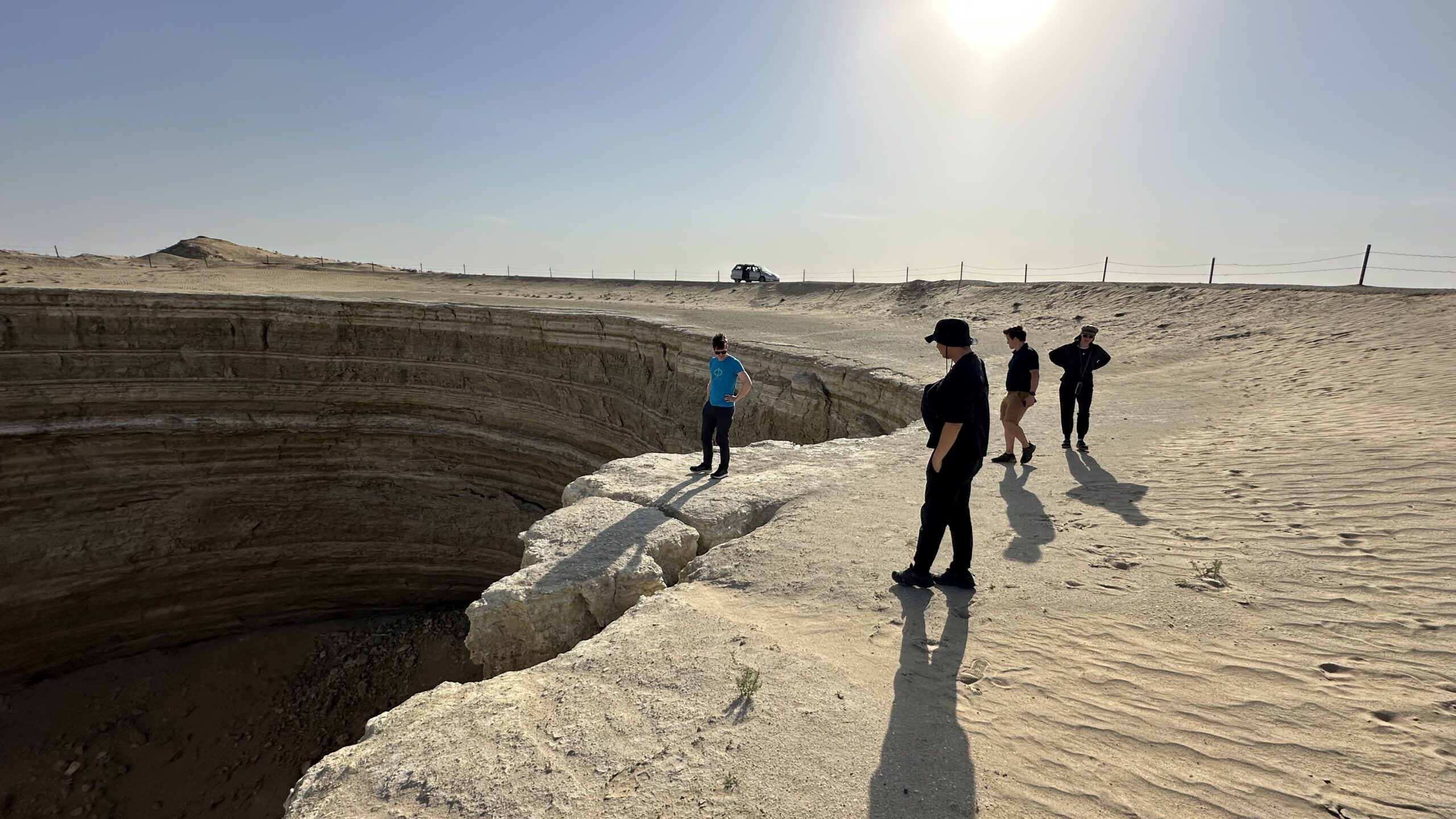 Travelers photographing the green water crater near Darvaza during a guided tour through the Karakum Desert