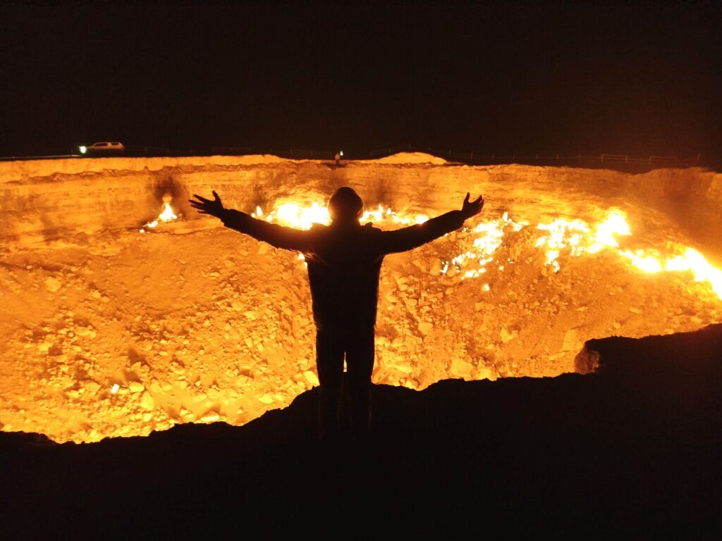 Silhouette of a person standing against the glowing Darvaza Gas Crater at sunset in Turkmenistan