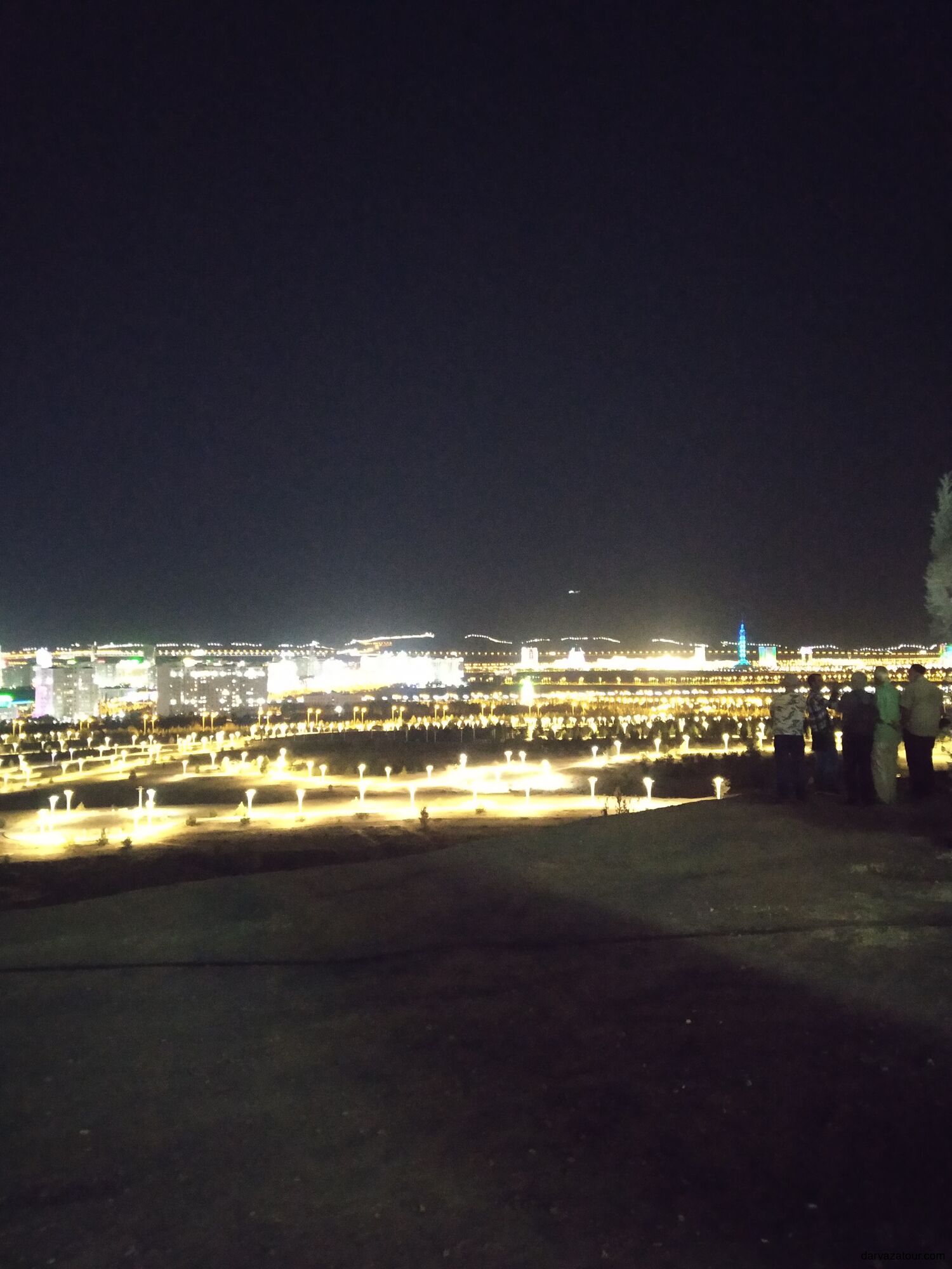 Four elderly travelers with guide enjoying panoramic night view of Ashgabat city from Bahkt Köşgi Hotel hill