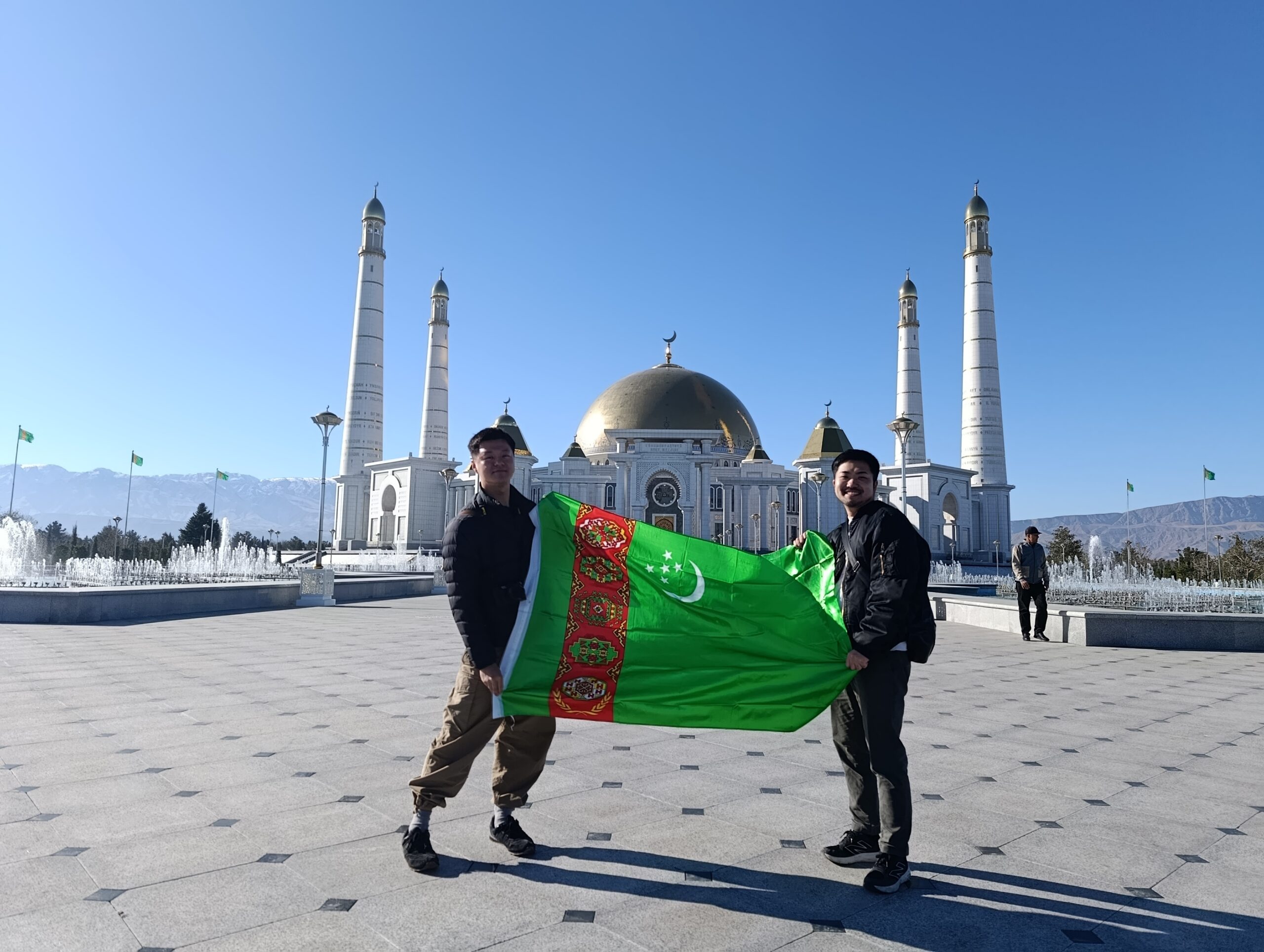 Two Japanese tourists holding the Turkmenistan flag in front of Turkmenbashi Ruhy Mosque