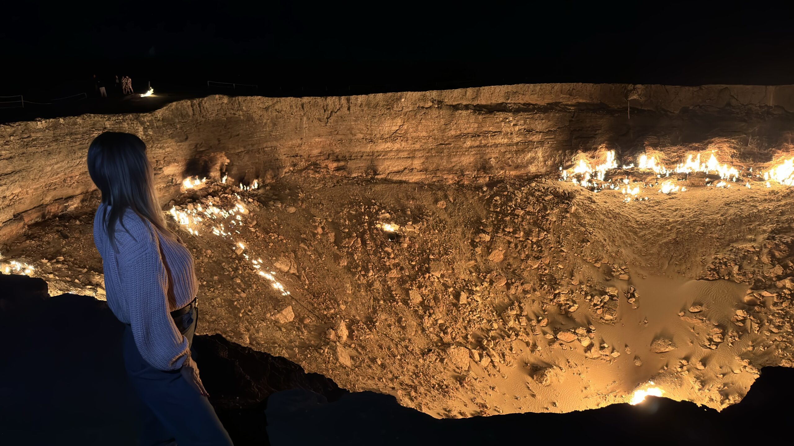 Panoramic Night View of Darvaza Gas Crater Russian traveler admiring a panoramic night view of the illuminated Darvaza Gas Crater in the Karakum Desert