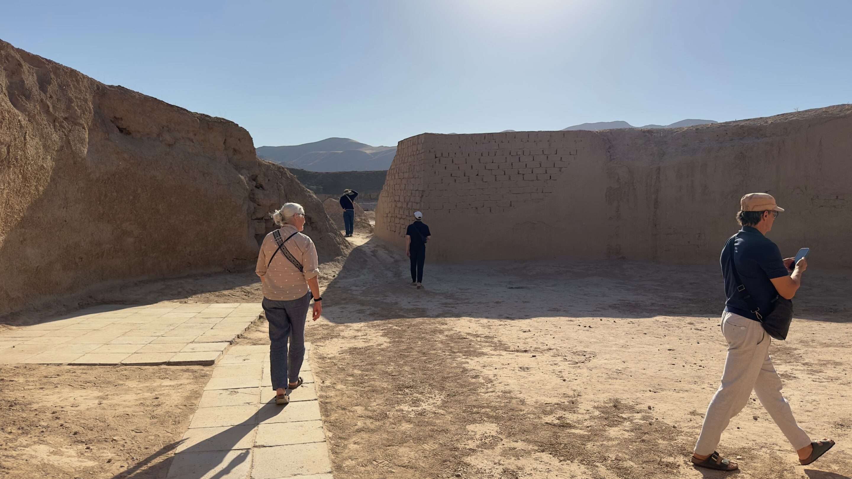 Travellers walking between the tall mud-brick walls of the Parthian palace complex at Old Nisa