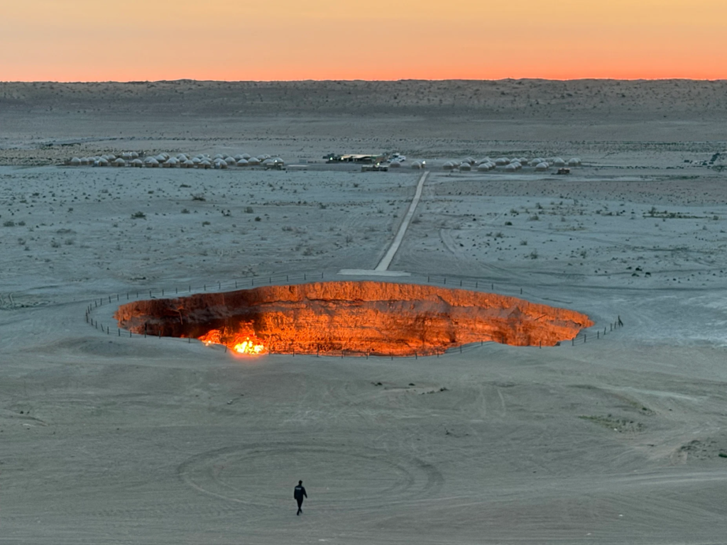Darvaza Gas Crater glowing in the early morning with the Darvaza yurt camp visible across the Karakum Desert at dawn