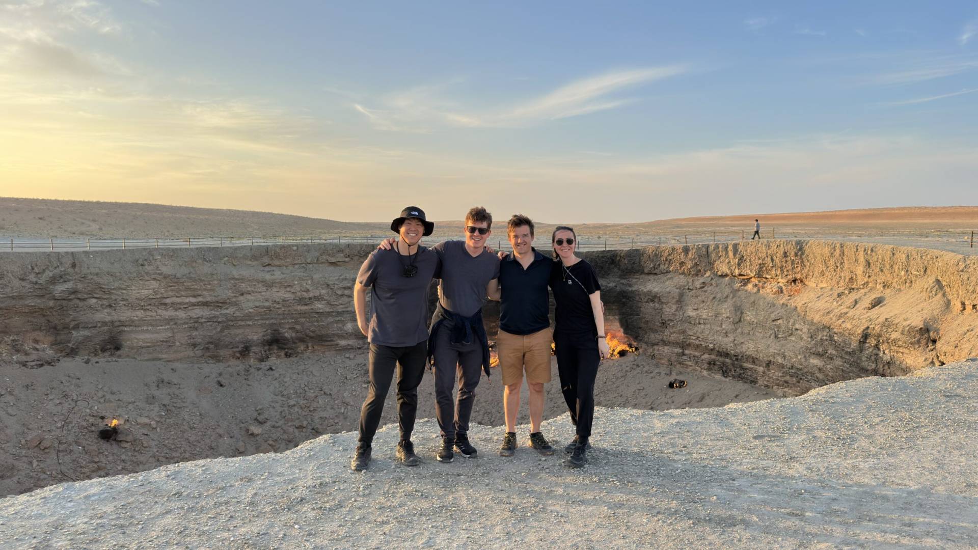 One Japanese traveler and three Belgian travelers posing together at Darvaza Gas Crater during a Turkmenistan group tour