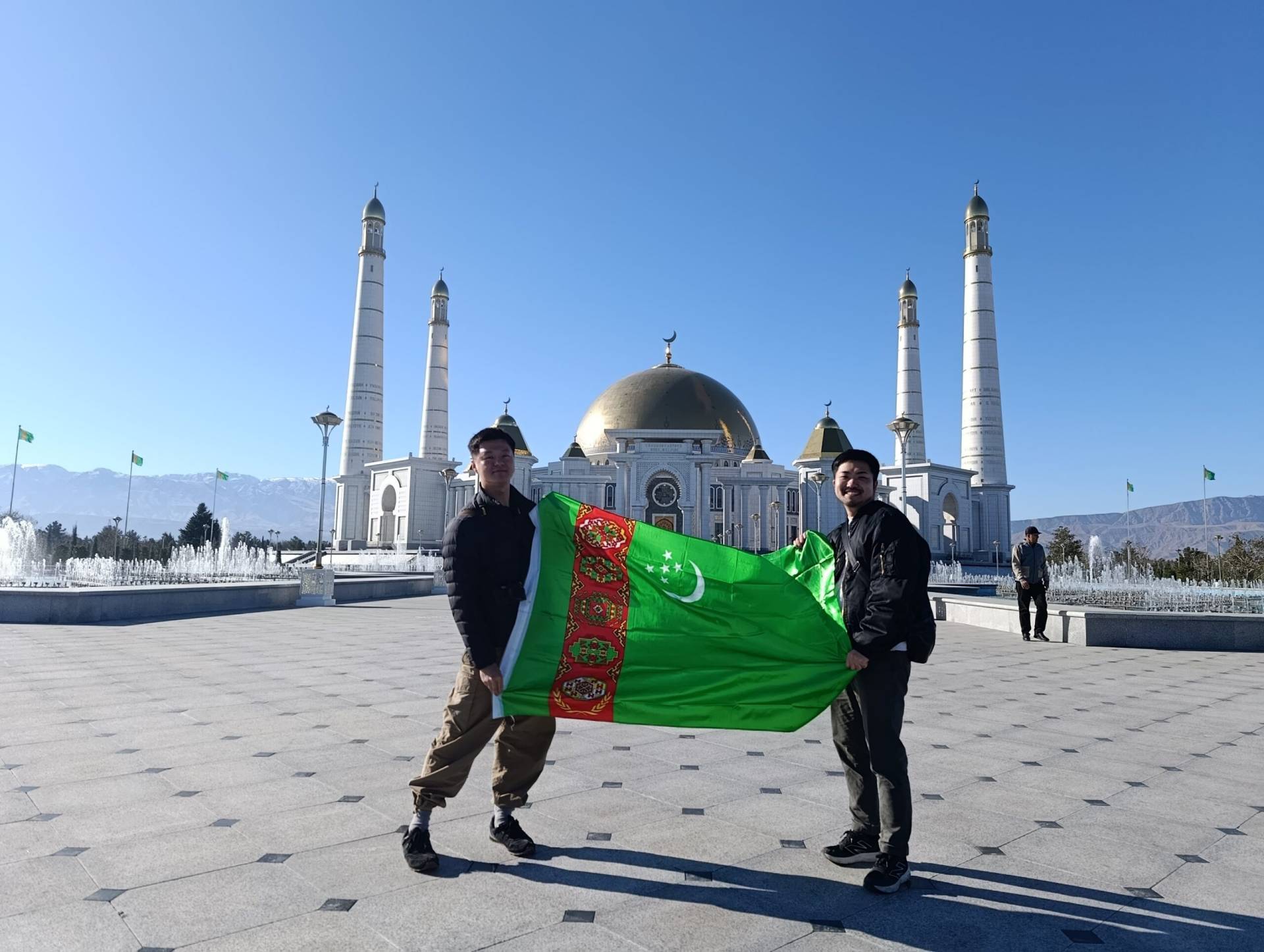 Two Japanese tourists holding the Turkmenistan flag in front of Turkmenbashi Ruhy Mosque
