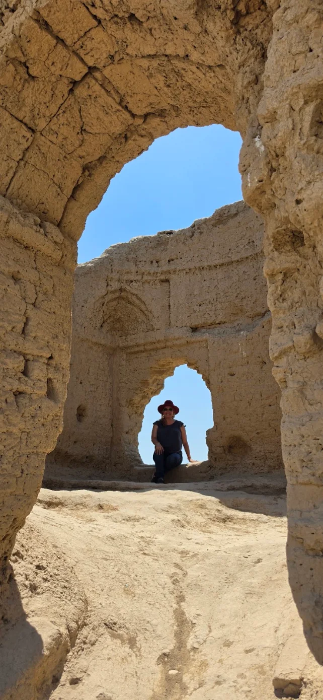 Traveler sitting inside the ancient mud-brick ruins of Little Kyz Kala at Merv, framed by historic arches beneath the blue Turkmenistan sky