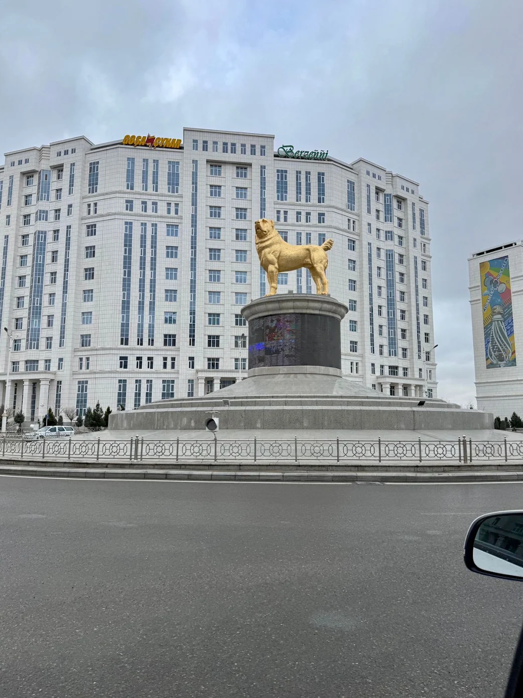 Golden Alabay dog monument in Ashgabat standing on a large pedestal surrounded by modern white buildings