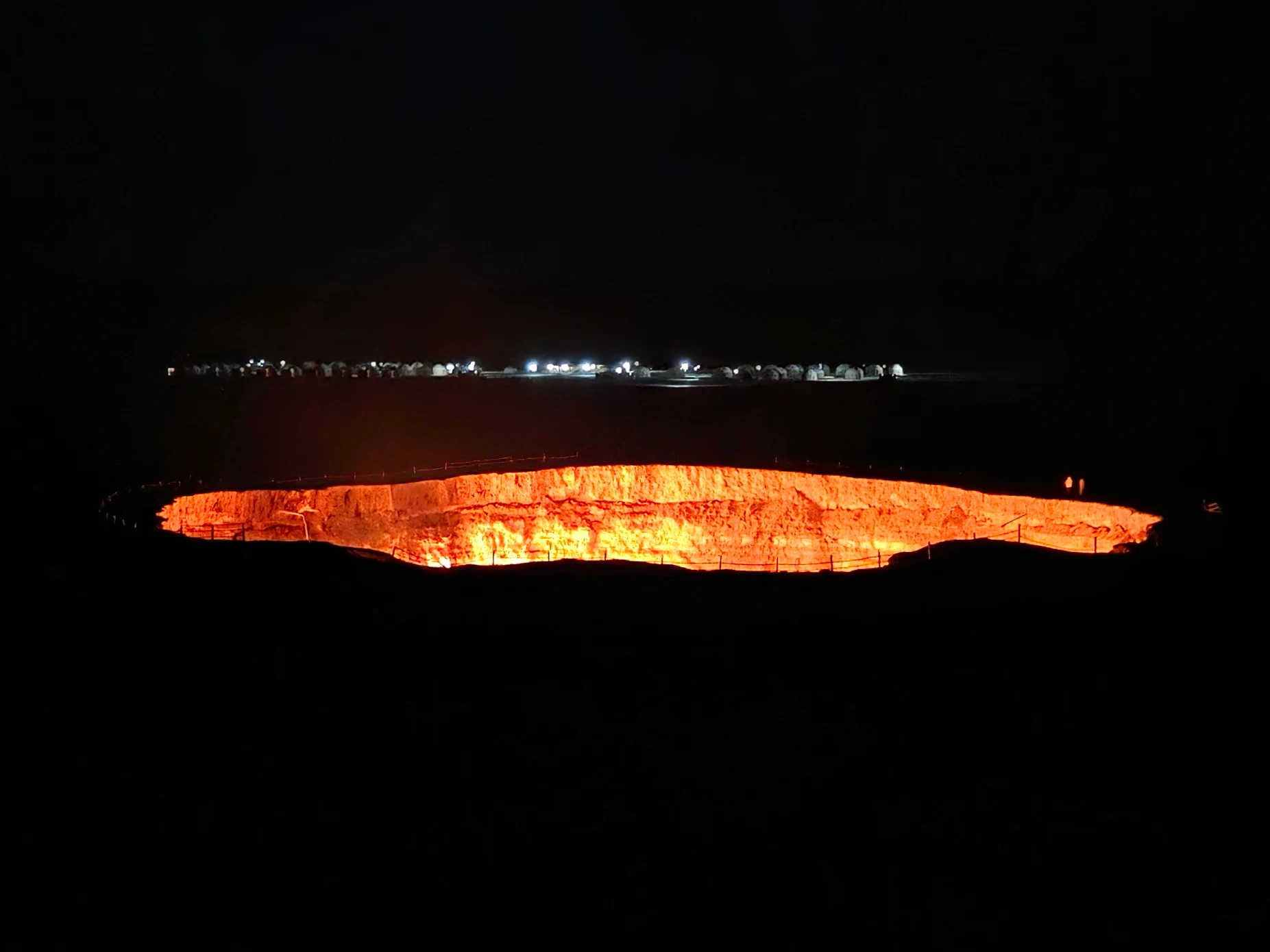 Burning Darvaza Gas Crater glowing in the darkness with the illuminated yurt camp visible across the Karakum Desert