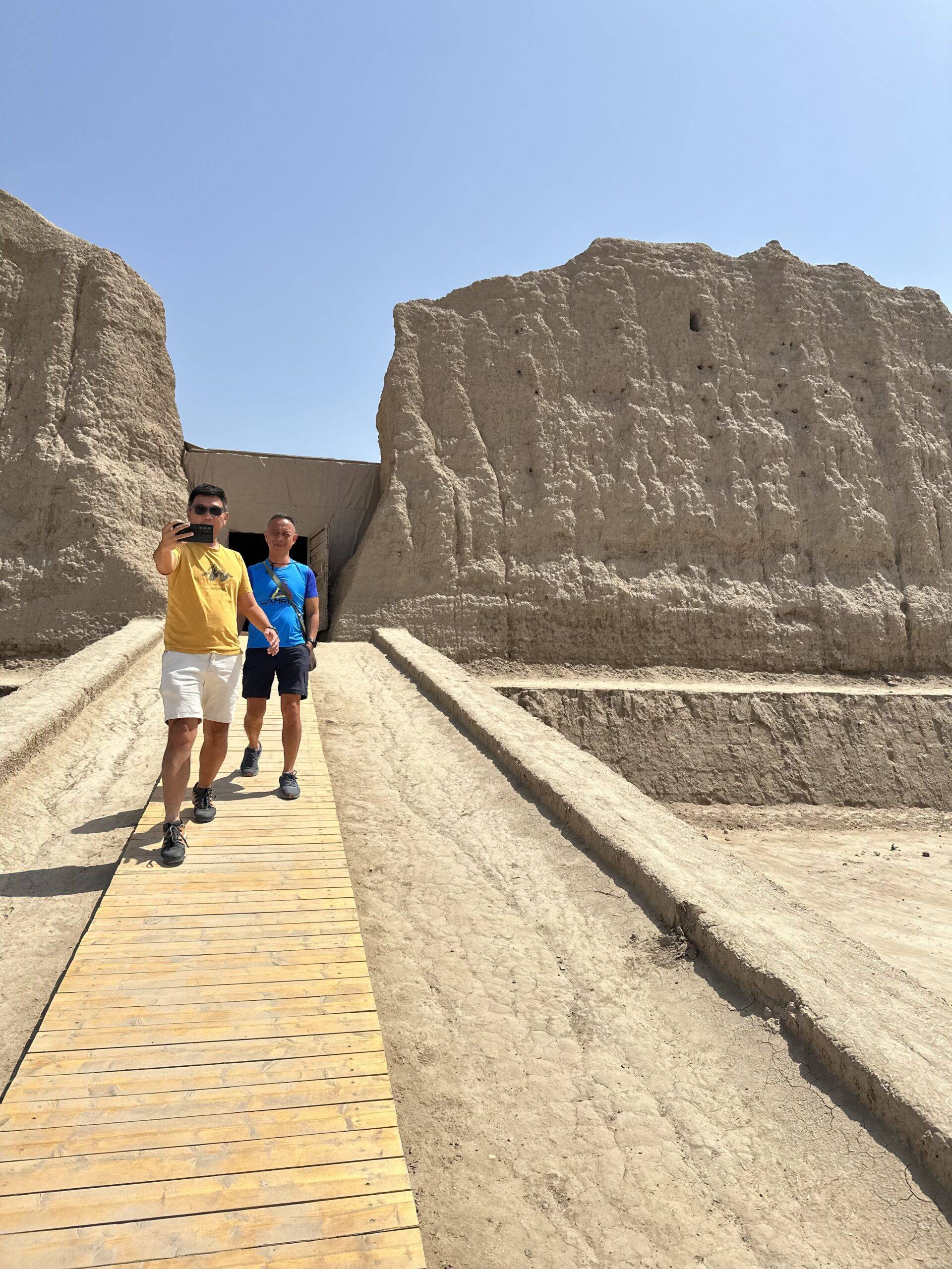 Two Malaysian travelers taking photos while leaving the monumental mud-brick ruins of Great Kyz Kala at Ancient Merv, Turkmenistan